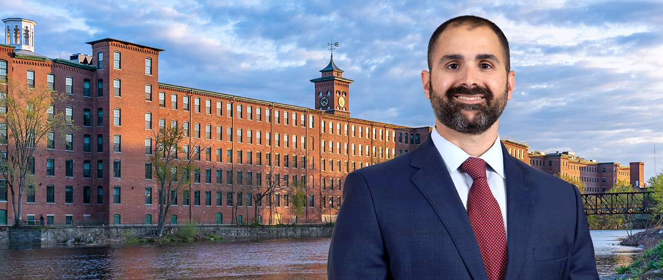 Attorney Joseph Russo before historic brick mill buildings along a river.