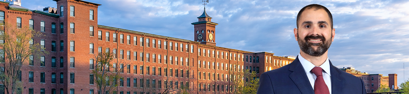 Attorney Joseph Russo before historic brick mill buildings along a river.